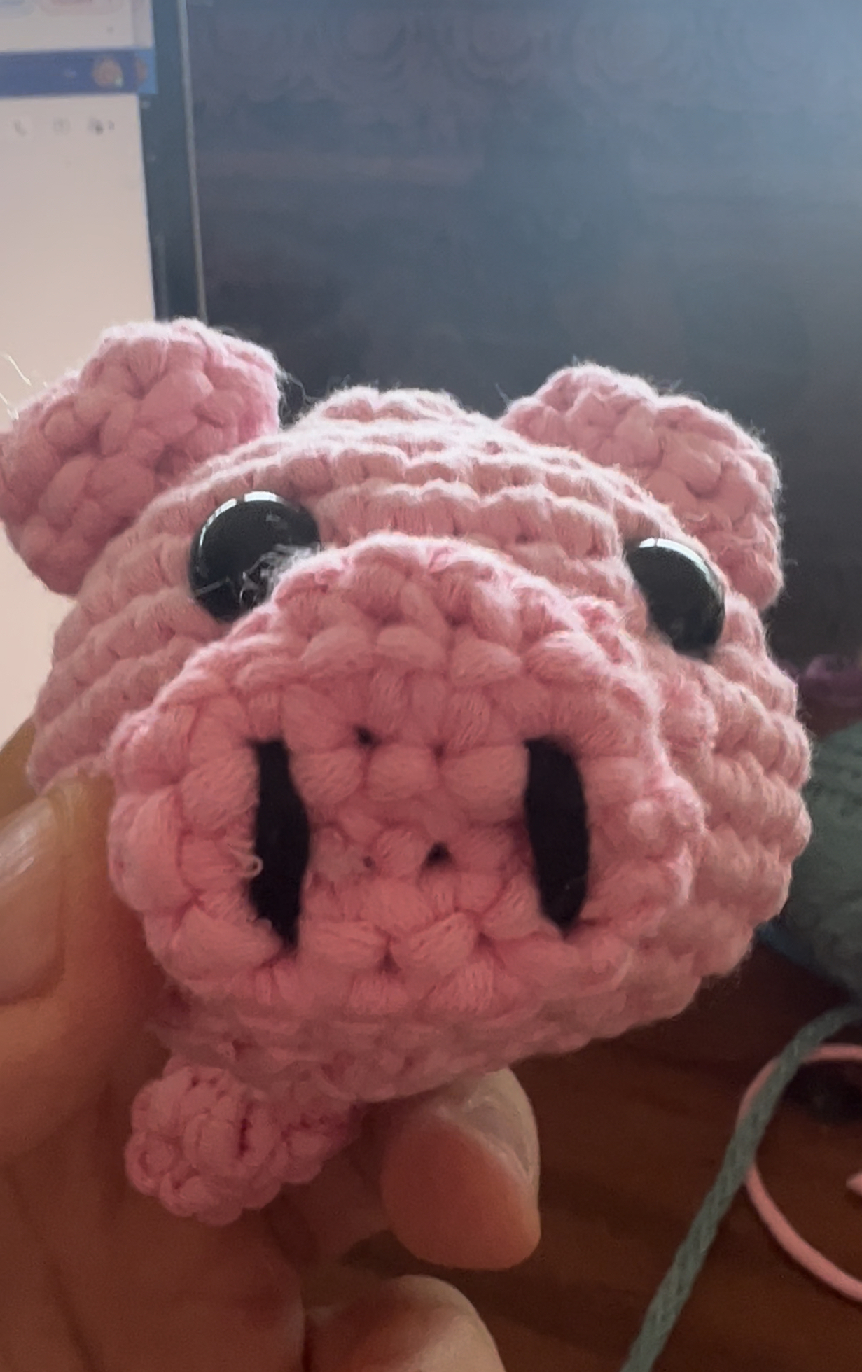 A small pink crocheted amigurumi pig with button eyes and a curly tail, held in a hand.