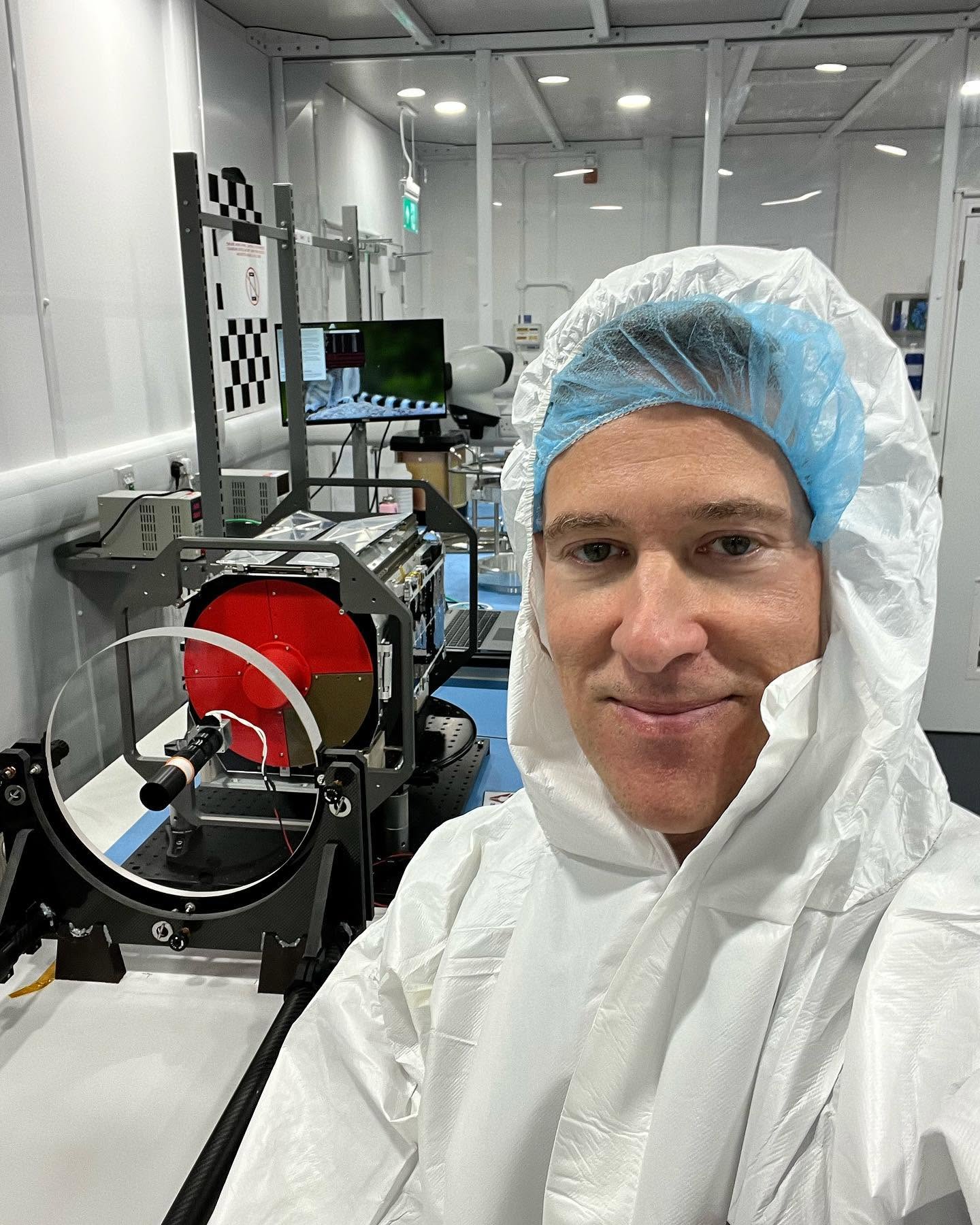 Andy in a cleanroom suit next to a Spire satellite